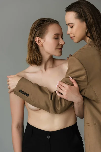 Brunette woman in beige blazer covering bust of lesbian girlfriend isolated on grey — Stock Photo