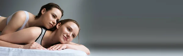 Happy lesbian woman looking away while lying near brunette girlfriend on grey background, banner — Stock Photo