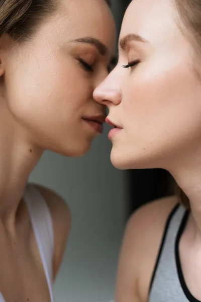 Vista lateral do casal lésbico com olhos fechados beijando no fundo cinza — Fotografia de Stock