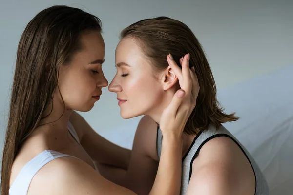 Vista lateral de sensual morena mujer tocando el pelo de joven lesbiana novia sobre fondo gris - foto de stock