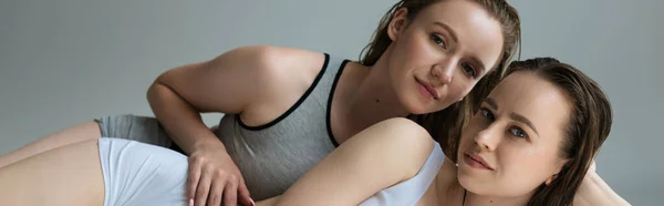Pareja de jóvenes y sexy lesbianas parejas en ropa interior mirando cámara aislada en gris, pancarta — Stock Photo