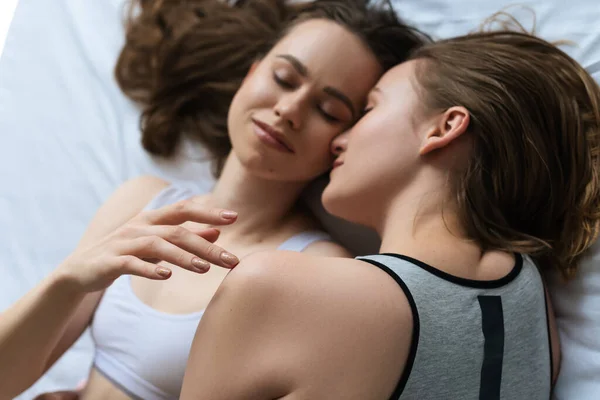 Draufsicht einer lächelnden lesbischen Frau, die mit geschlossenen Augen auf dem Bett liegt und junge Freundin berührt — Stockfoto