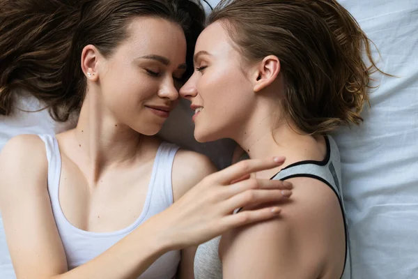Вид зверху усміхненої брюнетки жінка торкається лесбійської дівчини на ліжку — стокове фото