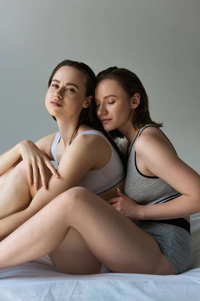 Sensual lesbian woman looking at camera while sitting near young girlfriend isolated on grey — Stock Photo