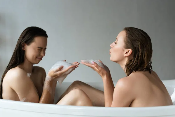 Вид збоку оголена лесбіянка пара розважається з мильною піною у ванній — стокове фото
