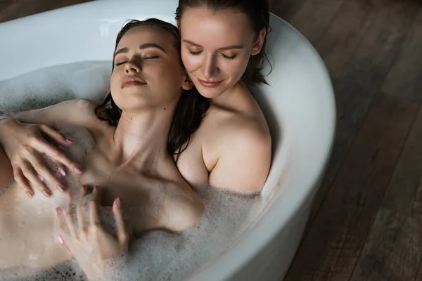 Вид зверху усміхненої жінки, що приймає груди лесбійської дівчини, приймаючи ванну разом — Stock Photo