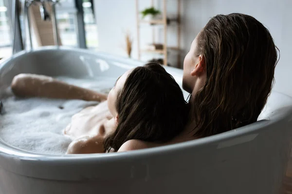 Vista trasera de las mujeres lesbianas jóvenes relajándose en baño de burbujas juntos - foto de stock