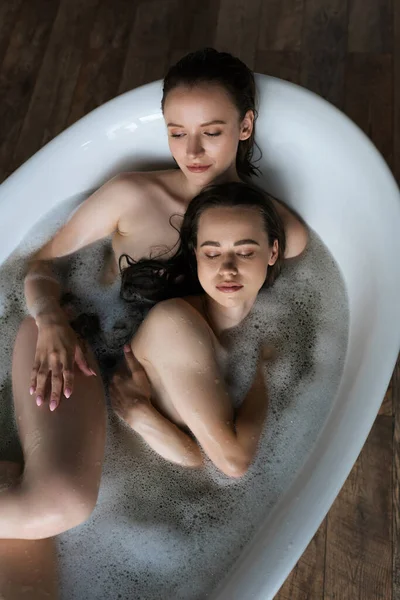 Вид зверху на молодих і голих лесбійських партнерів, що відпочивають у ванній вдома — стокове фото