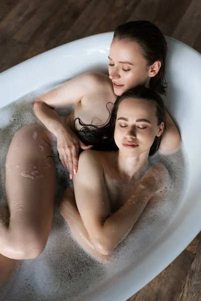 Vista superior de parejas lesbianas desnudas con los ojos cerrados bañándose en casa juntos - foto de stock