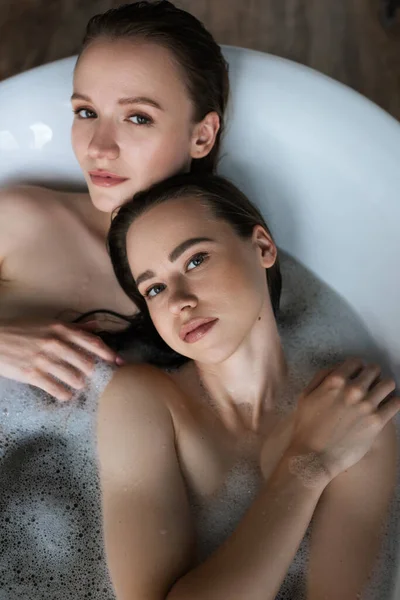 Вид зверху на молодих і красивих лесбійок, які приймають ванну і дивляться на камеру — стокове фото