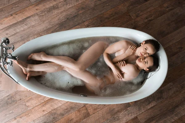 Vue supérieure du couple lesbien sexy embrassant dans la baignoire et regardant la caméra — Photo de stock