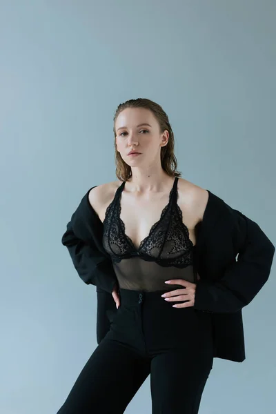 Young woman in black trousers and black lingerie standing with hands on hips isolated on grey — Stock Photo