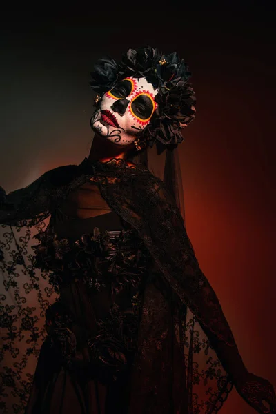 Woman in black wreath with veil and day of dead makeup looking at camera on burgundy background — Stock Photo