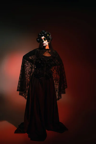 Mujer en traje negro y maquillaje de Halloween espeluznante de pie sobre fondo borgoña - foto de stock