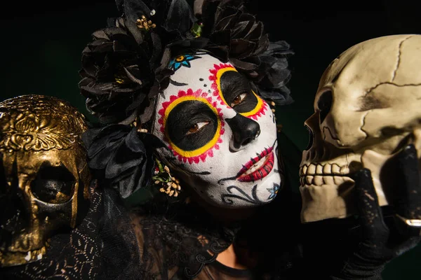 Femme en couronne noire et maquillage cartina tenant crânes isolés sur noir — Photo de stock
