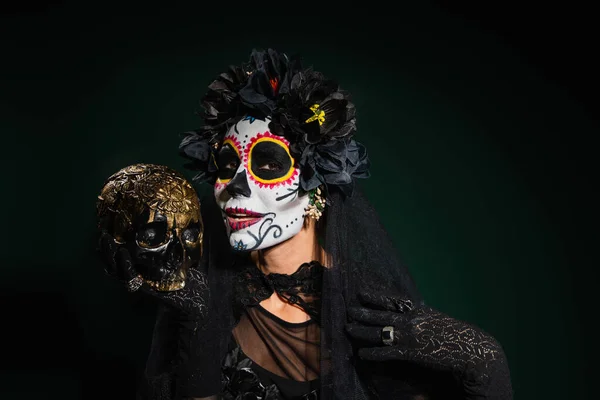 Femme souriante en costume santa muerte halloween tenant crâne sur fond vert foncé — Photo de stock