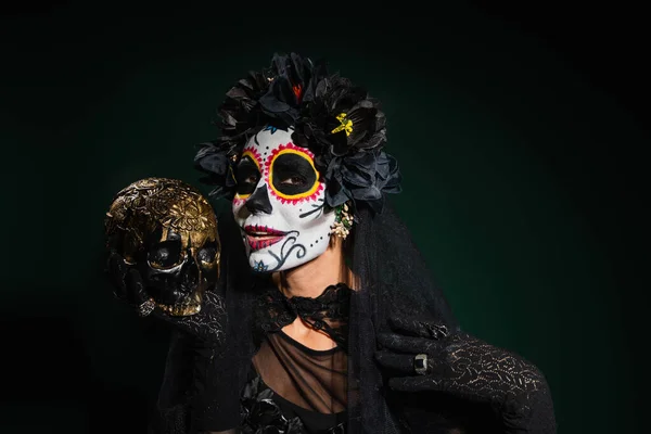 Sorrindo mulher em santa muerte halloween traje segurando crânio no fundo verde escuro — Fotografia de Stock