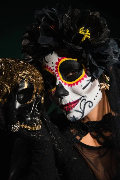 Portrait of woman in halloween catrina makeup and wreath holding skull isolated on black — Stock Photo