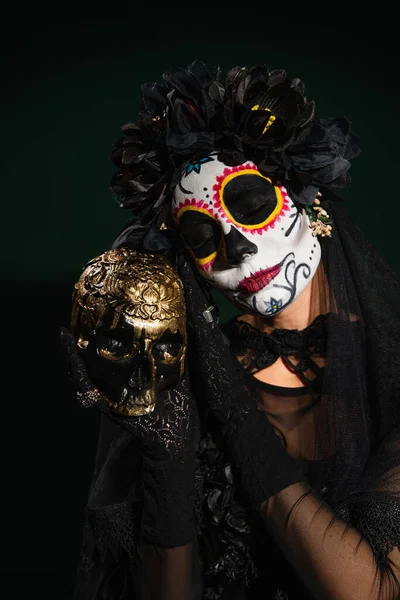 Portrait of woman in day of dead costume holding skull on dark green background — Stock Photo