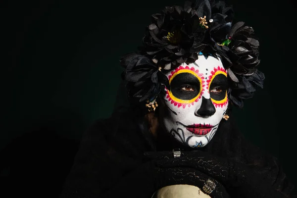 Mujer en maquillaje de catrina mexicana y corona con flores negras sobre fondo verde oscuro - foto de stock