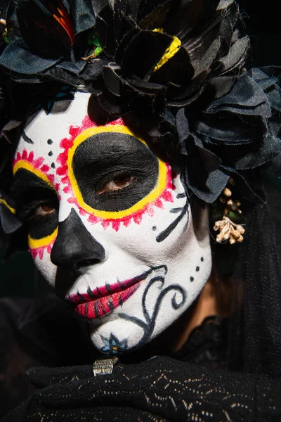Портрет женщины с сахарным макияжем черепа и темным венком, смотрящей на камеру, изолированную на черном — стоковое фото