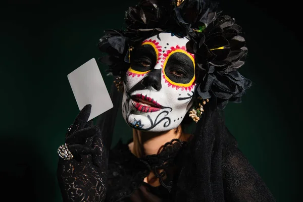 Retrato de mujer en traje de santa muerte y tarjeta de celebración de maquillaje aislado en verde oscuro - foto de stock