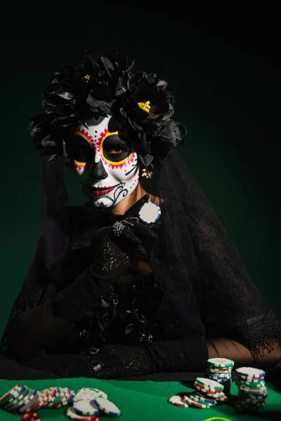 Mujer en traje de Halloween de santa muerte sosteniendo chip sobre fondo verde oscuro - foto de stock