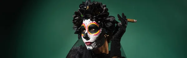 Donna con trucco Santa Muerte e ghirlanda che tiene sigaro su sfondo verde, banner — Foto stock