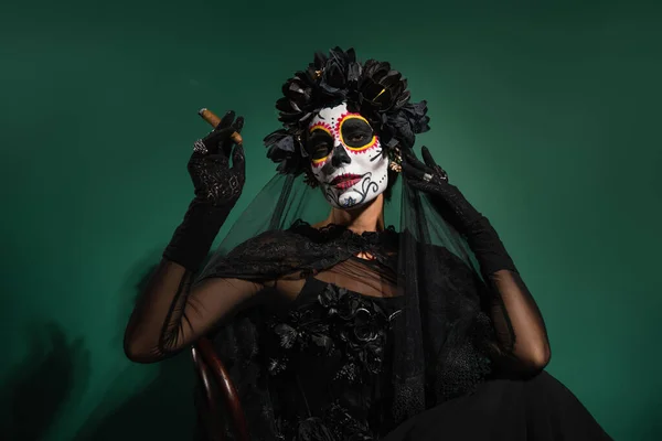 Femme avec costume santa muerte effrayant tenant cigare et posant sur fond vert — Photo de stock