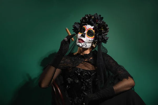 Woman in day of death halloween costume and black veil holding cigar on green background — Stock Photo