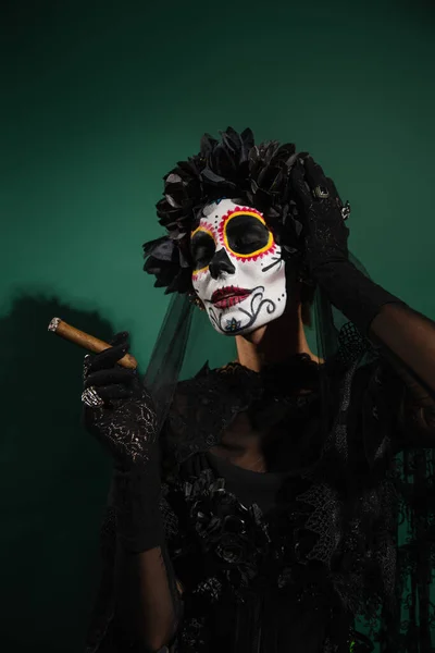 Женщина в мексиканский день мертвый макияж и костюм держа сигару на зеленом фоне — стоковое фото