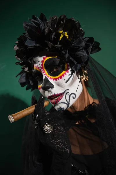 Portrait of woman in santa muerte halloween costume holding cigar on green background — Stock Photo