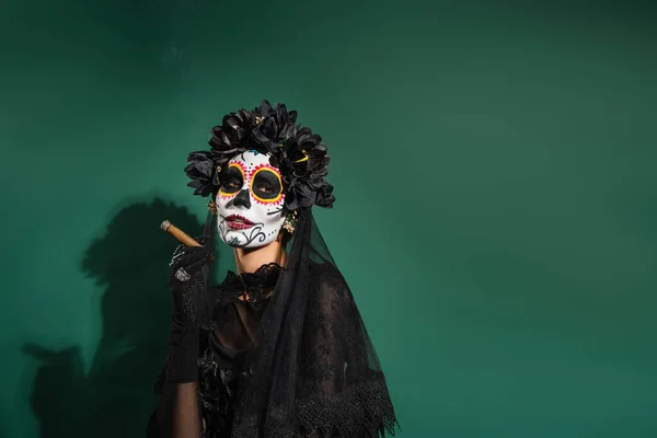 Mujer en el día de la muerte traje de Halloween celebración de cigarros sobre fondo verde - foto de stock