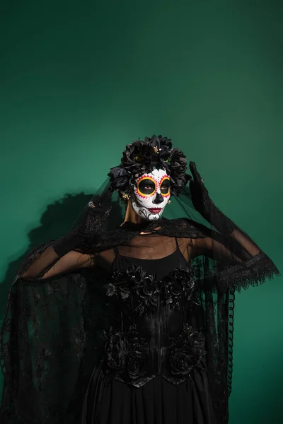 Mujer en traje espeluznante de santa muerte y maquillaje de pie sobre fondo verde - foto de stock