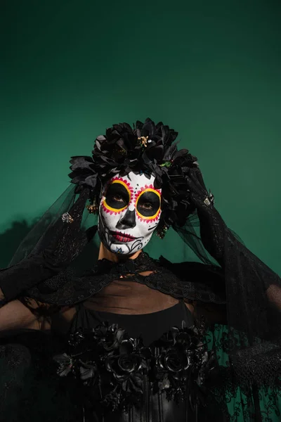 Mujer en traje de Halloween santa muerte y corona mirando a la cámara sobre fondo verde - foto de stock