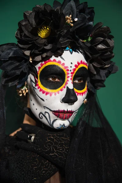 Mujer en corona negra y halloween día de la muerte maquillaje posando aislado en verde - foto de stock