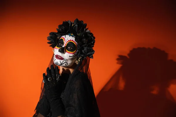 Frau in santa muerte Make-up und schwarzem Kostüm steht auf rotem Hintergrund — Stockfoto