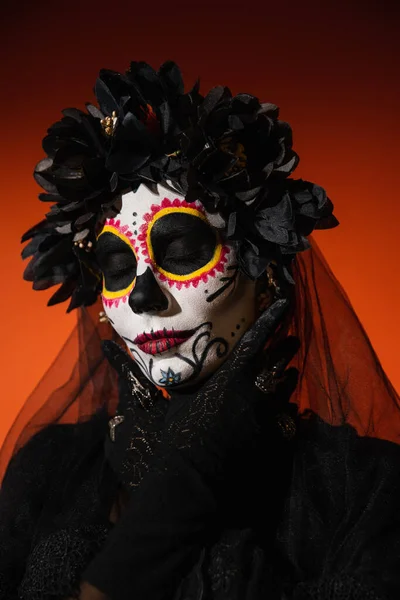 Retrato de mujer en traje de halloween y maquillaje de cráneo de azúcar posando sobre fondo rojo - foto de stock