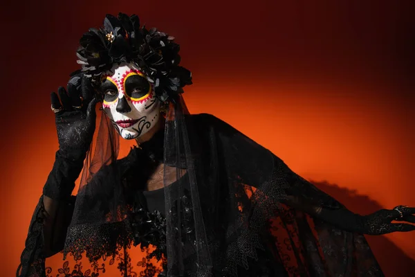 Frau mit Zuckerschädel-Halloween-Make-up und schwarzem Kostüm posiert auf rotem Hintergrund — Stockfoto