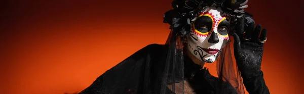 Женщина в костюме смерти в Хэллоуин позирует и смотрит в камеру на красном фоне, баннер — стоковое фото