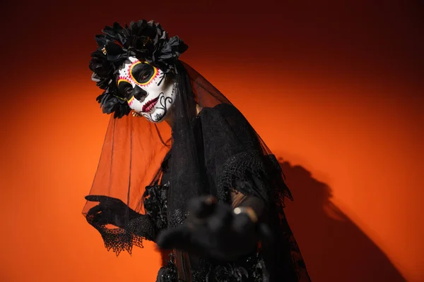 Mujer en traje de santa muerte y maquillaje espeluznante mirando a la cámara sobre fondo rojo - foto de stock