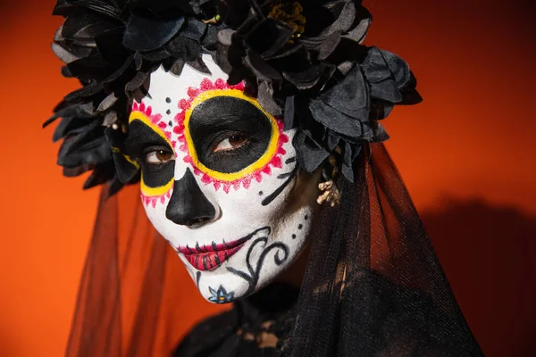 Retrato de mujer en maquillaje catrina y corona negra sobre fondo naranja con sombra oscura - foto de stock