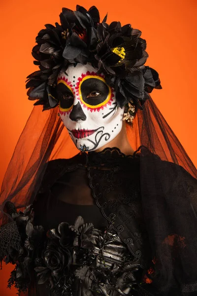 Mujer en día mexicano de maquillaje muerto y traje con corona negra y velo aislado en naranja - foto de stock