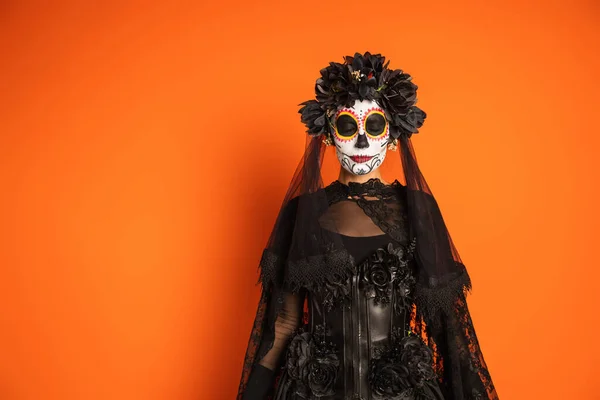 Mujer en traje de Halloween bruja y maquillaje espeluznante de pie con los ojos cerrados aislados en naranja - foto de stock