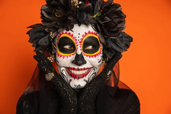Счастливая женщина в жутком сахарном черепе макияж глядя в сторону изолированы на оранжевый — стоковое фото