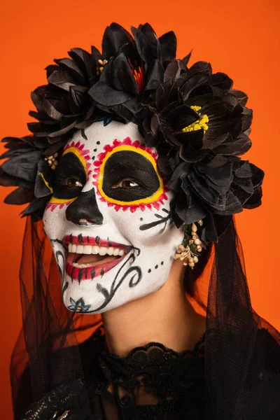 Портрет веселой женщины в страшном хэллоуинском макияже и черном венке с завесой, изолированной на оранжевом — стоковое фото