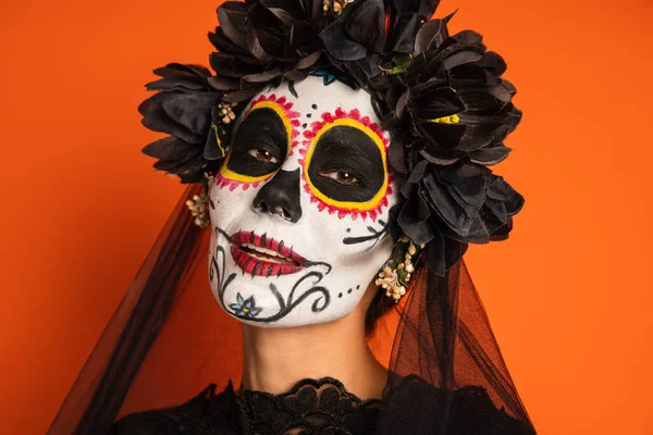 Retrato de mulher positiva em maquiagem de crânio de açúcar e coroa preta com véu isolado em laranja — Fotografia de Stock