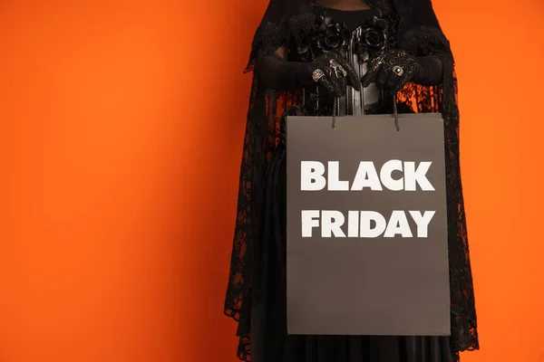 Cropped view of woman in spooky halloween makeup holding shopping bag with black friday lettering isolated on orange — Stock Photo