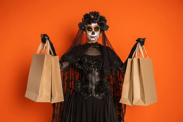 Donna in catrina trucco e giorno messicano di costume morto che mostra borse della spesa isolate su arancione — Foto stock
