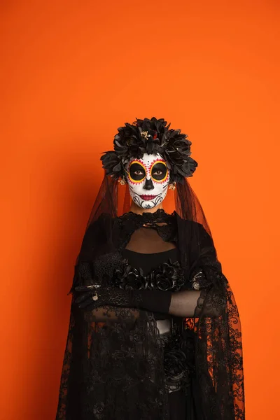 Femme en costume de sorcière noire et jour mexicain traditionnel de maquillage mort debout avec les bras croisés isolés sur orange, bannière — Photo de stock